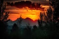 majestic mountain range, with fiery sunset in the background, and silhouettes of trees against the sky Royalty Free Stock Photo