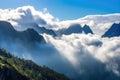 majestic mountain range, with misty clouds and sunshine, against blue sky Royalty Free Stock Photo