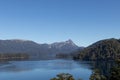 Majestic nature view of a huge clear blue lake reflecting the forest that surrounds it and the mountain range in the distance, in Royalty Free Stock Photo