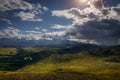 Majestic panorama of mountain plain on the background of snow-covered ridge before thunderstorm. Sun`s rays break through huge