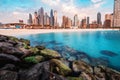 Rocks breakwaters in the foreground with the azure waters of the Persian Gulf and colorful skyscrapers in the Marina and