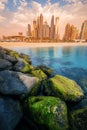 rocks breakwaters in the foreground with the azure waters of the Persian Gulf and colorful skyscrapers in the Marina and