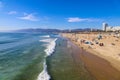 A majestic shot of the large waves breaking in vast blue ocean water with a sandy beach filled with people and the cityscape