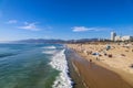 A majestic shot of the large waves breaking in vast blue ocean water with a sandy beach filled with people and the cityscape