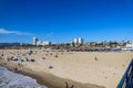 A majestic shot of the large waves breaking in vast blue ocean water with a sandy beach filled with people and the cityscape