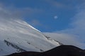 Majestic shot of a snow-covered mountain slope surrounded by clouds and a daytime full moon