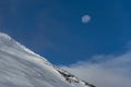 Majestic shot of a snow-covered mountain slope surrounded by clouds and a daytime full moon