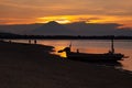 Majestic sunset on sea - golden sky, last sunbeams, dark volcano, black silhouette of fishing boat and walking people on beach. Royalty Free Stock Photo