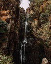 Majestic vertical shot of a rough rugged bush-covered cliff with a thin long waterfall