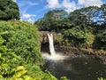 Majestic waterfall cascading over a large expanse of tranquil water with a rainbow above. Hawaii. Royalty Free Stock Photo