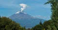 Majesty in Repose: A snow-capped volcano whispers smoke into the blue expanse as nature\'s silent sentinel