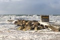 Major storm at the beach with huge crashing wave on a wooden and rocky groyne breakwater with ecume under a stormy sky