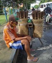 an old man selling a broom stick is sitting beside his bicycle waiting for a buyer