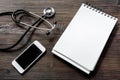 Make an appointment with doctor by cell phone dark wooden desk top view notebook mock up Royalty Free Stock Photo