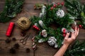Make christmas wreath. Hand hold spruce branches, cones, threads, sciccors on wooden background top view
