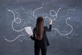 Make decision concept with back view on woman with paper in one hand writing on chalkboard