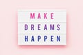 MAKE DREAMS HAPPEN written in light box on pink background. Motivation quote. Top view