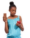 Make the healthy choice. a young african american girl trying to decide between eating an apple or an a piece of Royalty Free Stock Photo