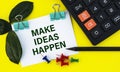 MAKE IDEAS HAPPEN - words on a white sheet with clips on a yellow background with a calculator, buttons and pencil