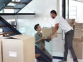 They make moving house look easy. Shot of a happy young couple passing boxes to each other while moving into their new