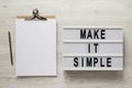 `Make it simple` words on a lightbox, clipboard with blank sheet of paper on a white wooden background, overhead view. Top view, Royalty Free Stock Photo