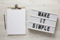 `Make it simple` words on a lightbox, clipboard with blank sheet of paper on a white wooden surface, overhead view. Top view, fr Royalty Free Stock Photo