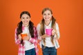 Make sure kids drink enough water. Girls kids hold cups orange background. Sisters hold mugs. Drinking tea while break