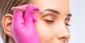 Make-up artist plucks eyebrows with tweezers to a woman before staining with henna.Makeup concept, eyebrow shape modeling and Royalty Free Stock Photo