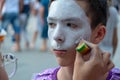 Street makeup for a celebration of Halloween or a costume show. Close-up. Make-up artist`s hand puts white paint on the face of a