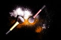 Make-up brushes with colorful powder on black background. Explosion stars dust with bright colors. White and orange powder.
