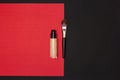Make-up foundation bottle with flat makeup brush on red and black background. Top view, copy space