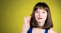 Make-up. brunette doing eyebrow makeup looking in mirror on yellow background.