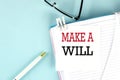 MAKE A WILL text on a sticky on notebook with pen and glasses , blue background