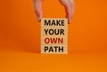 Make your own path symbol. Wooden blocks with words `Make your own path`. Male hand. Beautiful orange background. Business and Royalty Free Stock Photo