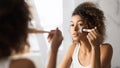 Afro Woman Applying Face Powder With Makeup Brush In Bathroom
