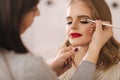 Makeup artist applies eye shadow, perfect evening makeup. Beauty blond hair girl with perfect skin and red lipstick Royalty Free Stock Photo