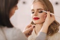 Makeup artist applies eye shadow, perfect evening makeup. Beauty blond hair girl with perfect skin and red lipstick Royalty Free Stock Photo