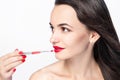 Makeup artist does makeup to a beautiful young woman. Brush red lipstick. Female beauty portrait on the white background