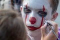 Street makeup for halloween. A makeup artist paints a clown`s face to a teenager guy like Pennywise. A man in the image of IT on