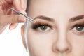 Makeup artist plucks the eyebrows of a beautiful woman in the beauty salon. Face close up.