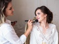 Makeup artist preparing beautiful bride before the wedding in a morning Royalty Free Stock Photo