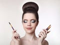 Makeup artist. Pretty teen girl with cute bun hairstyle and fashion beauty makeup, brunette holding brushes in hand isolated on w