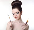 Makeup artist. Pretty teen girl with cute bun hairstyle and fashion beauty makeup, brunette holding brushes in hand isolated on w