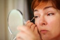 Makeup beauty care woman. Adult woman looks into mirror and putting eye pencil color on eyes