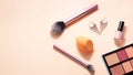 makeup and beauty supplies (brushes, eyeshadow palette, nail polish, earrings) on orange background