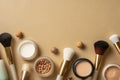 Makeup brushes and cosmetics on a beige background, top view with copy space