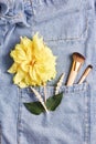 Makeup brushes and hair clips on denim background. creative concept. yellow Dahlia flower. top view, flat lay, vertical frame Royalty Free Stock Photo