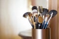 Makeup brushes in metal stand over blurred abstract room background