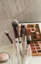 Makeup brushes stand in a glass against a background of makeup shadows