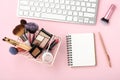 Makeup cosmetic products with notebook and keyboard on pastel pink desk